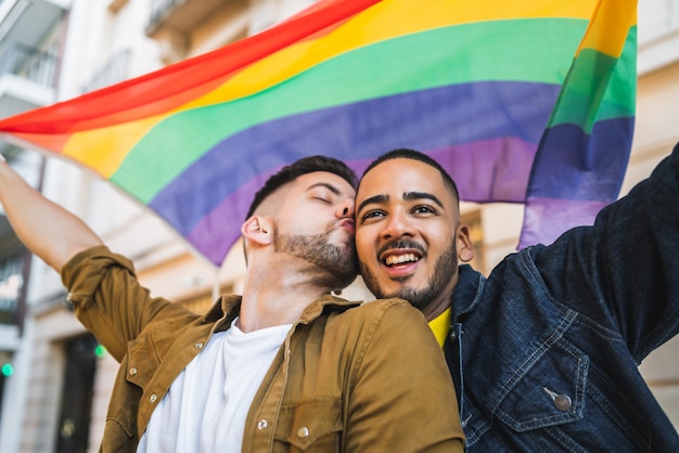 Coppia gay abbracciando e mostrando il loro amore con la bandiera arcobaleno.