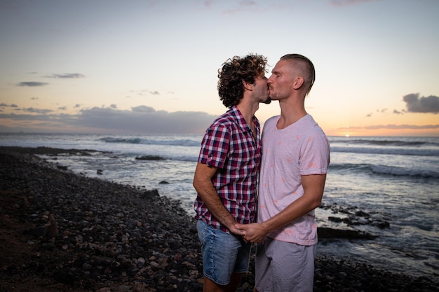 Coppia gay che si bacia in spiaggia durante il tramonto in estate Coppia dello stesso sesso in vacanza partner innamorati Momento romantico e passionale Concetto di coppia gay di San Valentino