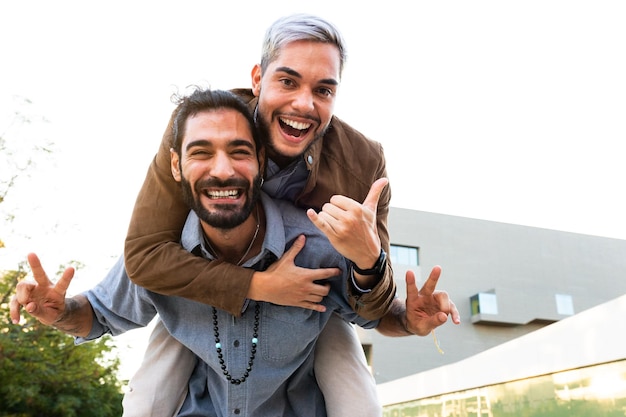 Coppia gay maschio sorridente allegro che guarda l'obbiettivo. L'uomo cavalca sulle spalle con il fidanzato. Copia spazio. concetto LGBT.