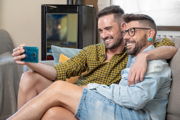 Coppia gay seduta sul divano a casa che fa videochiamata sul telefono cellulare