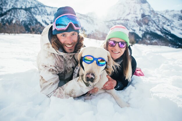 coppia giocando con il cane in montagna, sul terreno innevato