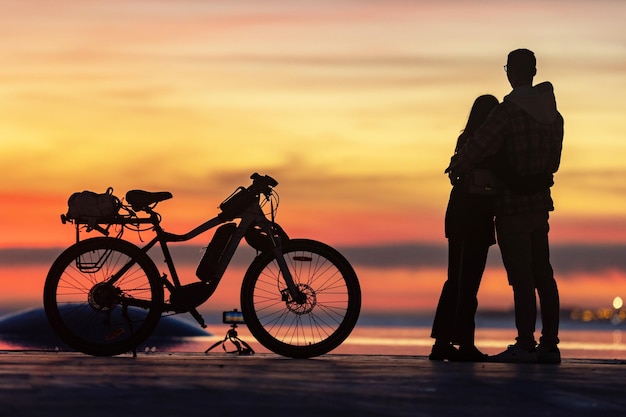 Coppia giovane abbracciare e guardare il tramonto in piedi da una bicicletta