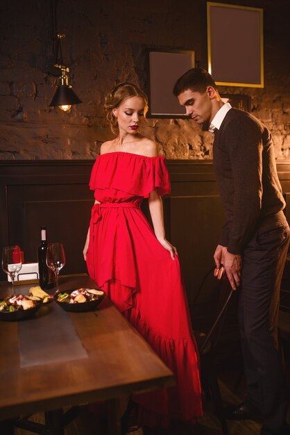 Coppia giovane amore nel ristorante, appuntamento romantico. Elegante donna in abito rosso e il suo uomo da pranzo