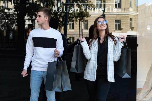 Coppia giovane con acquisti dopo lo shopping di successo. Venerdì nero. Ragazzo e ragazza con borse della spesa accanto alla vetrina.