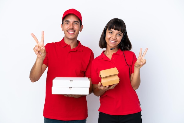 Coppia giovane consegna in possesso di pizze e hamburger isolati su sfondo bianco sorridente e mostrando il segno di vittoria