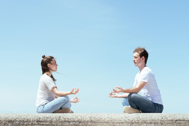 Coppia giovane meditando insieme in una giornata di sole con uno sfondo di cielo blu.