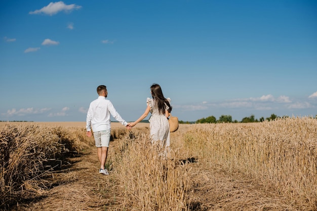 Coppia giovane nel campo di grano in una soleggiata giornata estiva. Le coppie innamorate si divertono in campo dorato. Coppia romantica in abiti casual all'aperto sul campo sconfinato