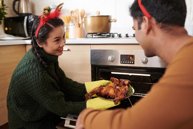 Coppia giovane prendendo pollo alla griglia sfornato per servire per la cena di Natale