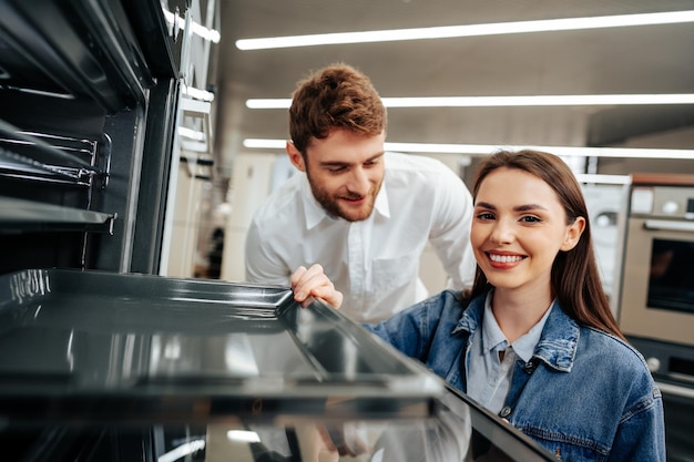 Coppia giovane scegliendo un nuovo forno elettrico in un ipermercato