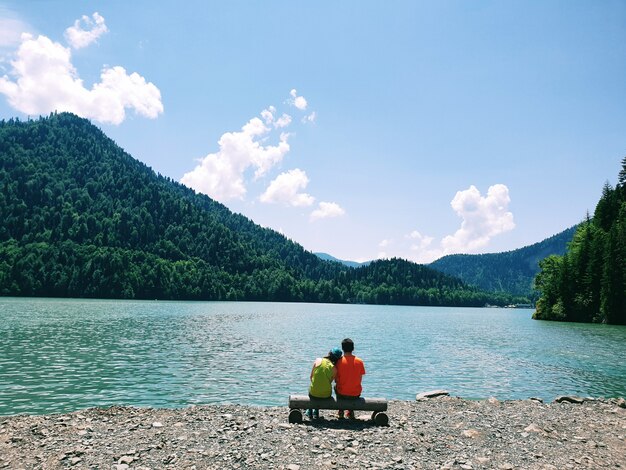 Coppia giovane seduto su una panchina a sfondo del lago Ritsa in Abkhazia in estate giornata di sole