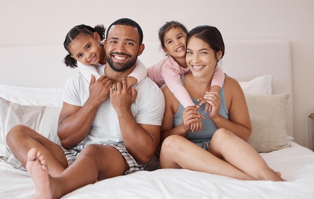 Coppia giovane sorriso sul letto con i bambini nella loro casa o appartamento Felice famiglia multiculturale in camera da letto con bambini piccoli durante le vacanze del fine settimana o le vacanze insieme per il ritratto