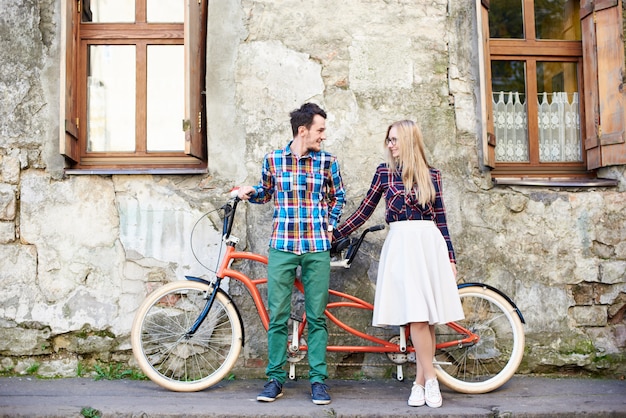 Coppia giovane turista, bell'uomo e bella donna bionda in sella a una bicicletta tandem lungo la strada cittadina.