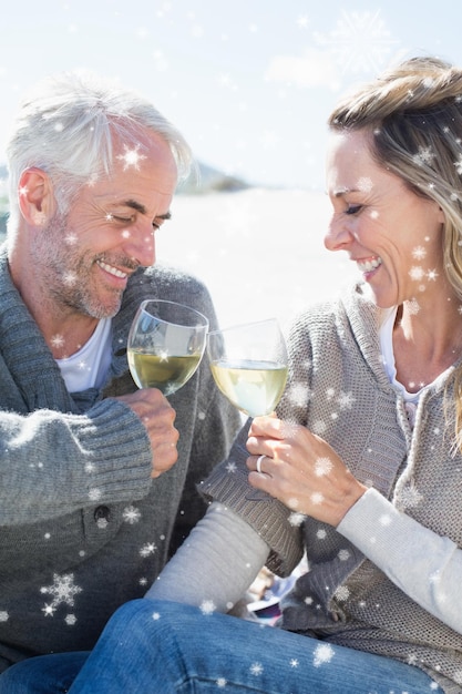 Coppia godendo di vino bianco sul picnic in spiaggia sorridendo a vicenda contro la neve che cade