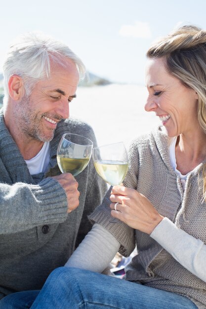 Coppia godendo vino bianco sul picnic in spiaggia sorridendo a vicenda