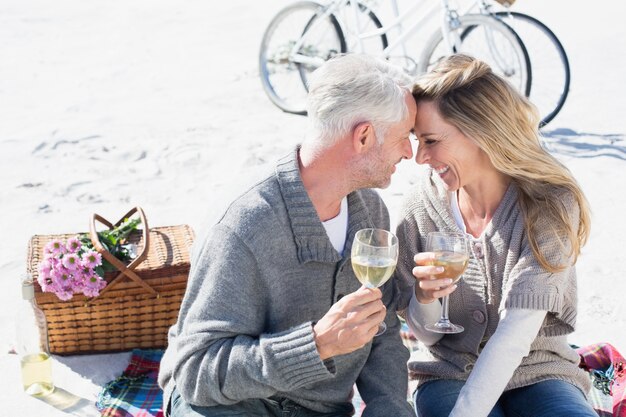 Coppia godendo vino bianco sul picnic in spiaggia sorridendo a vicenda