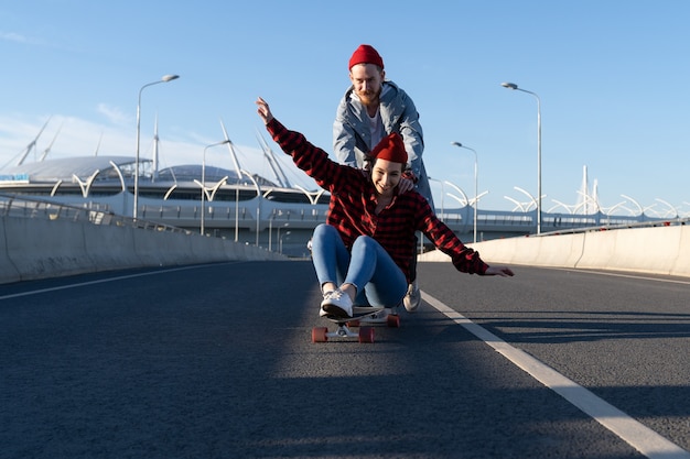 Coppia hipster spensierata che fa skateboard insieme uomo e donna alla moda si diverte a cavalcare il longboard