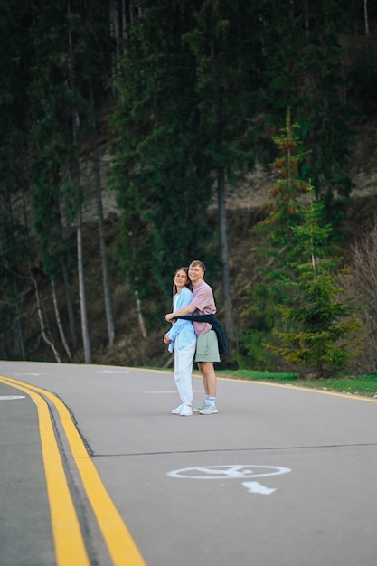 coppia in abiti casual eleganti in piedi su una strada di montagna in braccio e in posa per la fotocamera
