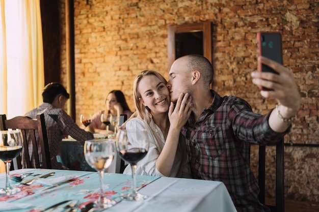 Coppia in amore prendendo un selfie mentre l'uomo bacia la moglie nel ristorante.