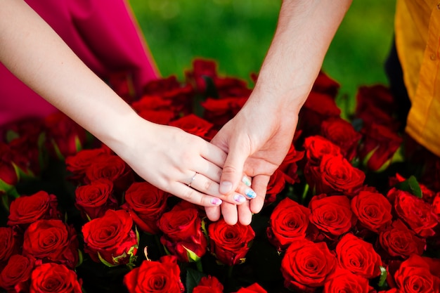 coppia in amore tenendosi per mano sopra un mazzo di rose rosse