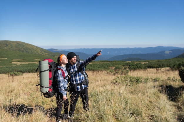 Coppia in amore turisti uomo e donna stanno su una pianura di montagna indicando con una mano lo spazio vuoto