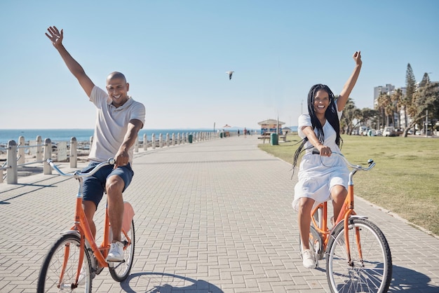 Coppia in bicicletta e celebrare la felicità per la libertà in spiaggia viaggio vacanza e vacanze estive Felice uomo donna sorriso e ciclismo bici allegro e ridendo insieme per amore sul marciapiede dell'oceano