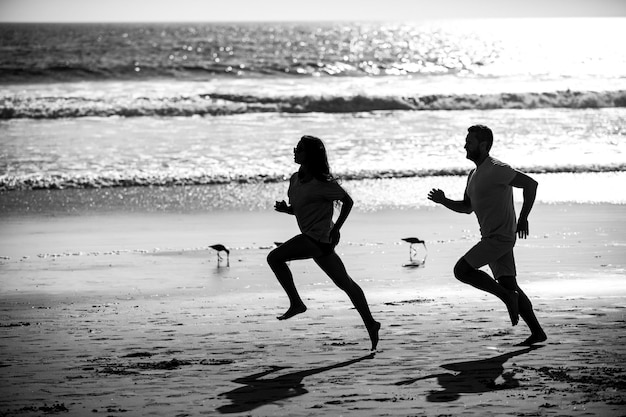 Coppia in esecuzione sulla spiaggia Silhouette di giovane uomo e donna che corre a fare jogging lungo il mare