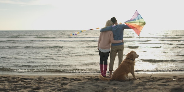 Coppia in esecuzione sulla spiaggia tenendo le mani con il cane il giorno dell'autunno