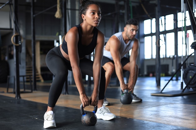 Coppia in forma e muscolare concentrata sul sollevamento di un manubrio durante una lezione di ginnastica in palestra.