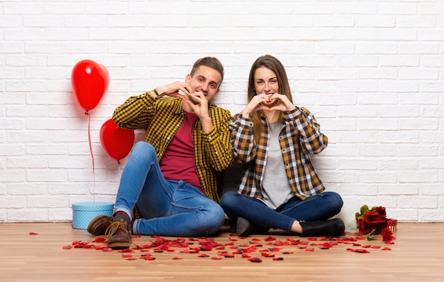 Coppia in giorno di San Valentino al chiuso facendo simbolo del cuore a mano