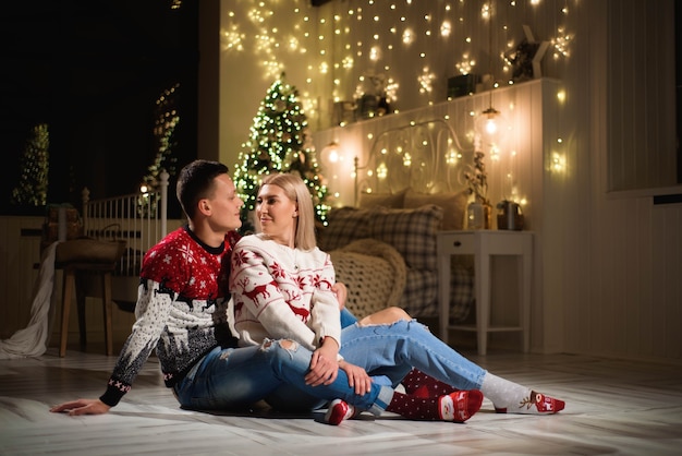 Coppia in maglioni a maglia vicino all'albero di Natale. Uomo e donna nella stanza interna di Natale.