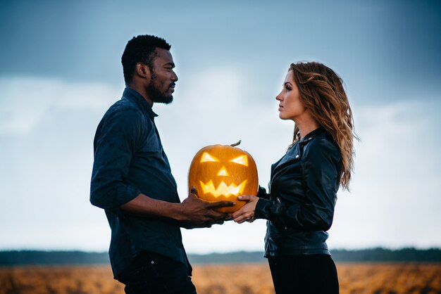 Coppia in piedi nel campo di zucca e tenendo zucca faccia spaventosa, concetto halloween