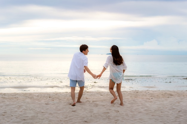 coppia innamorata avendo romantici momenti teneri in esecuzione e tenere la mano sulla spiaggia tra il tramonto