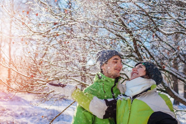 Coppia innamorata che getta neve e abbraccia nella foresta invernale Giovani che si divertono