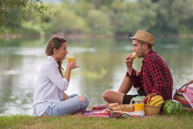 Coppia innamorata che si gode il tempo del picnic, beve e mangia nella splendida natura sulla riva del fiume