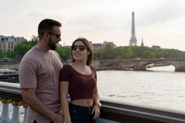 Coppia innamorata guardandosi e sorridendo con la torre eiffel sullo sfondo al tramonto da un ponte a parigi