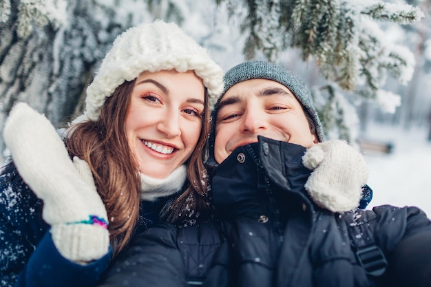 Coppia innamorata prendendo selfie e abbracciando nella foresta invernale innevata Giovani felici che si divertono il giorno di San Valentino