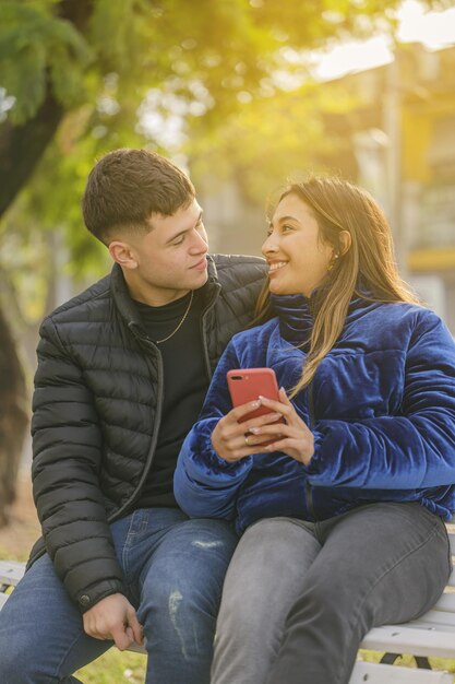 Coppia innamorata seduta su una panchina in un parco pubblico con il cellulare