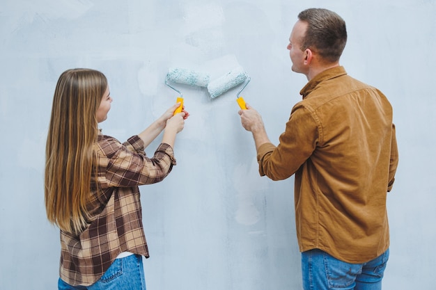 Coppia innamorata sposi novelli in camicie e jeans in una stanza vuota dipingendo pareti bianche e rinnovando l'interno Un uomo e una donna si sono trasferiti in una nuova casa Focus selettivo