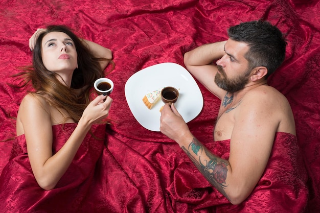 Coppia innamorata su lenzuola rosa scuro Uomo e donna con corpi semicoperti bevono caffè Mattina perfetta e concetto d'amore Ragazzo con la barba e fa colazione romantica con una donna sognante a letto vista dall'alto