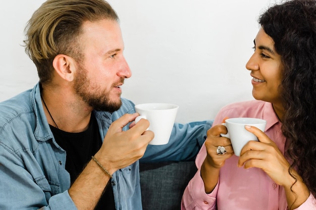 Coppia interrazziale seduta a bere caffè e sorridente.