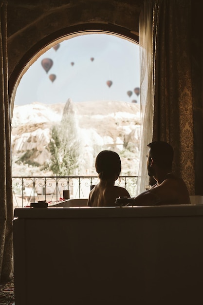 Coppia irriconoscibile facendo un bagno in hotel davanti a una finestra con mongolfiere che volano sullo sfondo del paesaggio Cappadocia Turchia