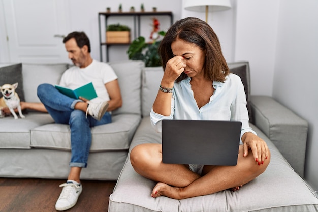 Coppia ispanica di mezza età a casa donna che usa il portatile stanca di strofinare il naso e gli occhi sensazione di stanchezza e mal di testa stress e frustrazione concetto