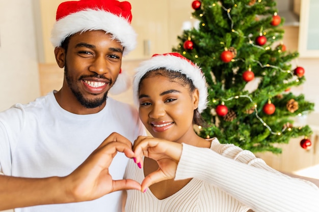 Coppia ispanica latina che mostra la forma del cuore dalle mani vicino all'albero di natale a casa