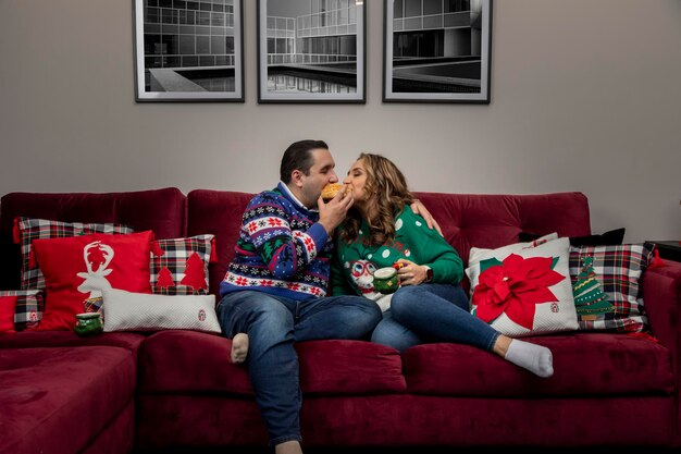 Coppia latina a Natale che mangia pane nel loro soggiorno con decorazioni natalizie e immagini ...