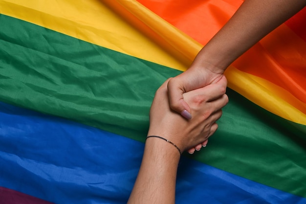 Coppia lesbica di due giovani donne che si tengono per mano sulla bandiera dell'orgoglio LGBT