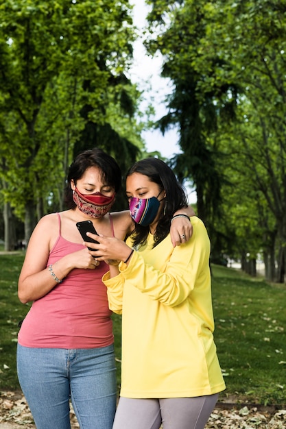 Coppia lesbica latina lesbica che sms con tecnologia smartphone e maschera facciale durante la pandemia di covid19 giovane giallo e lavanda LGTBQ