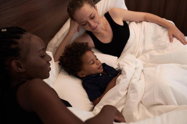 Coppia lesbica sdraiata a letto con il figlio piccolo e in attesa che si addormenti