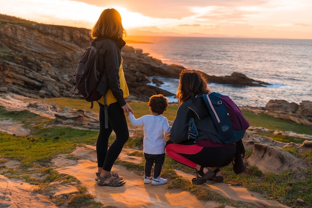 Coppia lgbt di donne con un bambino che guarda il tramonto sulla costa in riva al mare stile di vita familiare