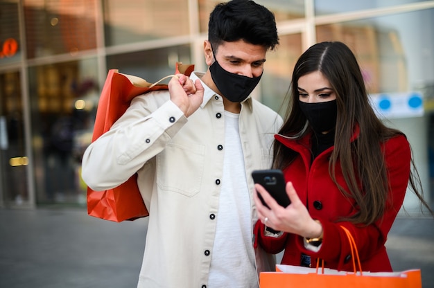 Coppia mascherata che fa shopping in un mercato di strada e usa uno smartphone che indossa maschere, concetto di coronavirus covid