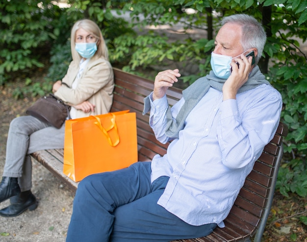 Coppia matura seduta ai lati di una panchina per mantenere le distanze durante i tempi del coronavirus